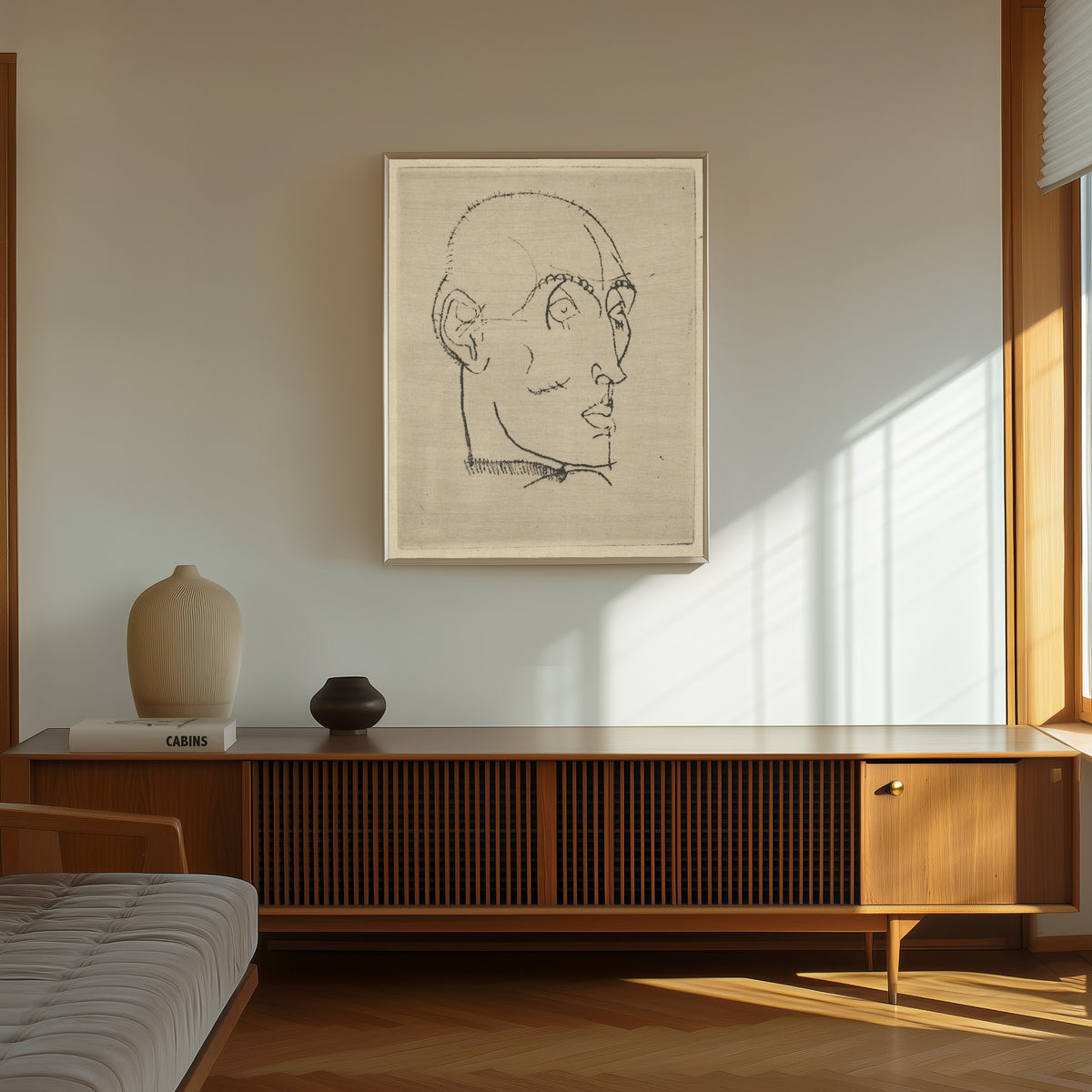 Framed art print of Portrait of a Man by Egon Schiele, in a thin light frame on a sunlit wall above a wooden sideboard