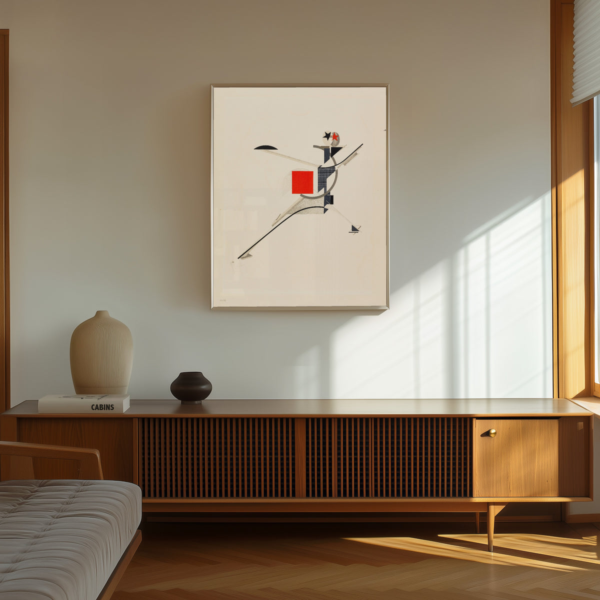 Framed art print of Figurines: The New Man (Neuer) by El Lissitzky, in a thin light frame on a sunlit wall above a wooden sideboard
