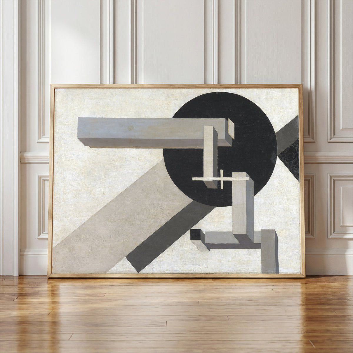 Framed art print of Proun 1D by El Lissitzky, in a light wood frame leaning against a panelled white wall