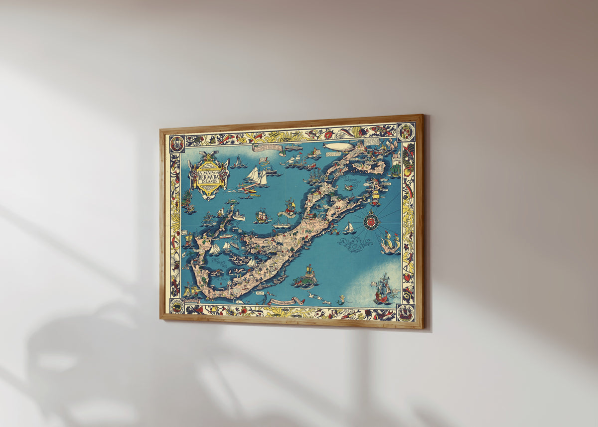 Framed art print of A Map of the Bermuda Islands by Elizabeth Shurtleff, in a light wood frame on a sunlit white wall, seen at a slight angle