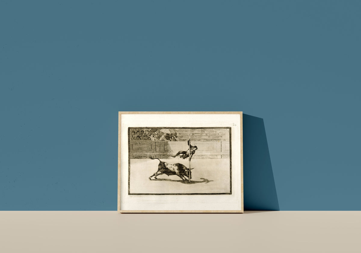 Framed art print of Ligereza y atrevimiento de Juanito Apiñani en la de Madrid (The Agility… by Francisco de Goya, in a light wood frame leaning on a blue wall