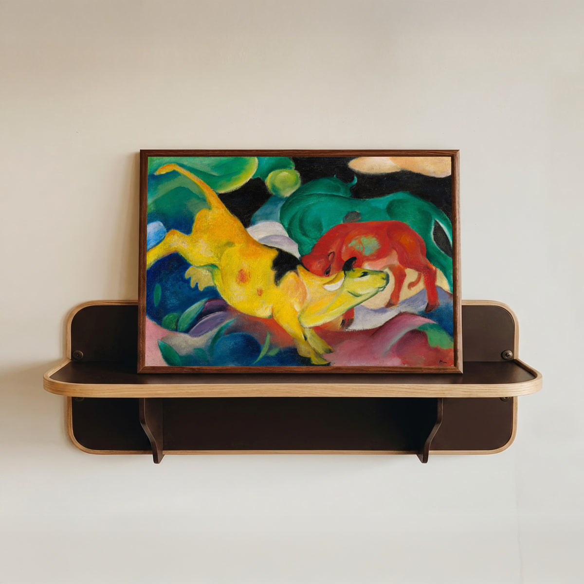 Framed art print of Cows, Red, Green, Yellow by Franz Marc, in a dark wood frame resting on a wall shelf