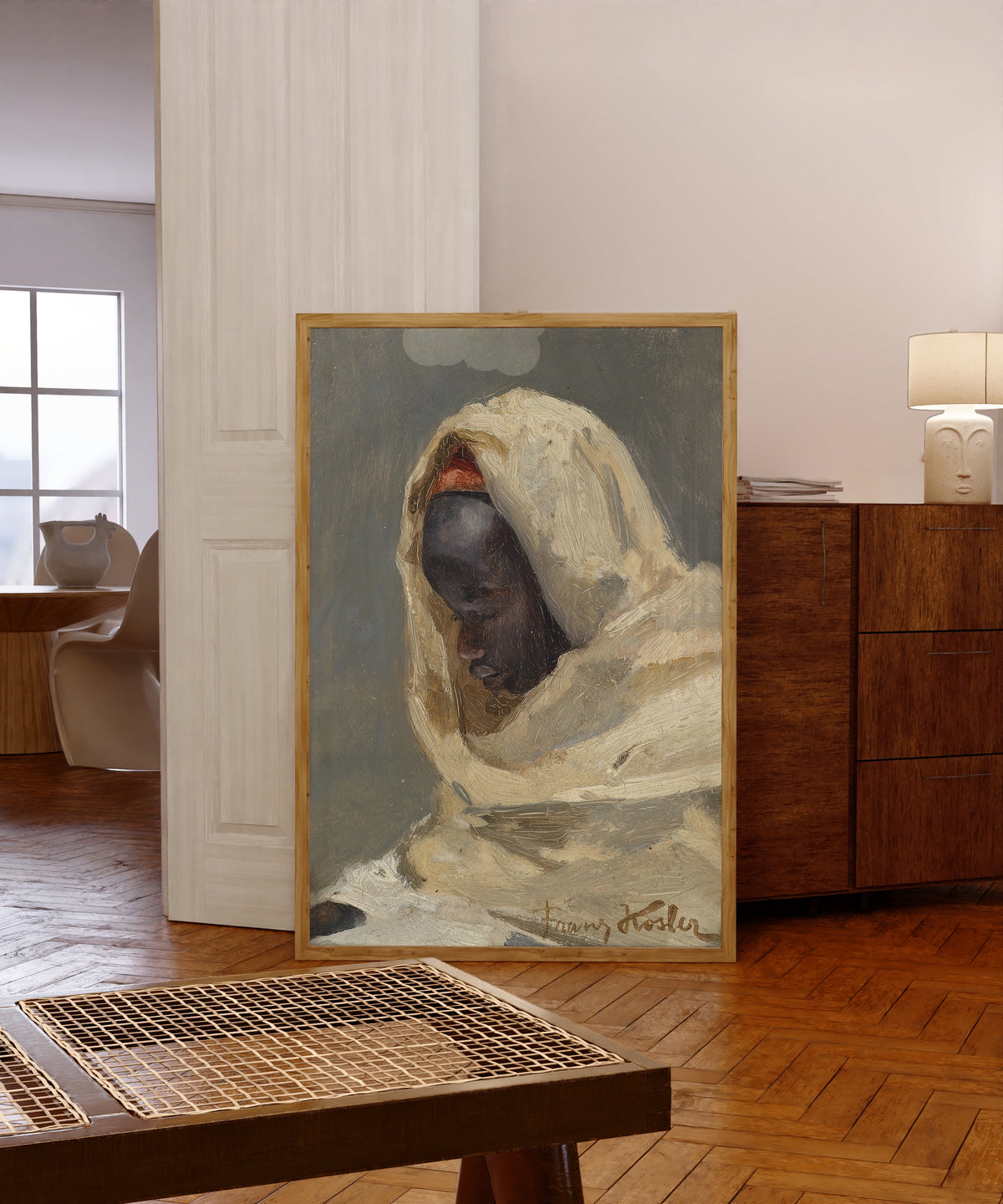 Framed art print of A Bedouin Man by Franz Xaver Kosler, in a light wood frame leaning in a warm room with a parquet floor