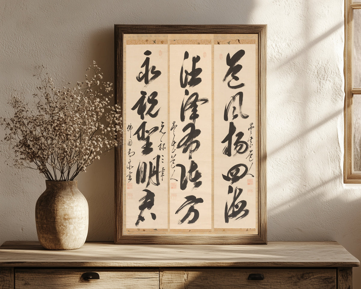 Framed art print of Calligraphy Triptych by Gaoquan Xingdun, in a dark wood frame leaning on a rustic console beside dried flowers