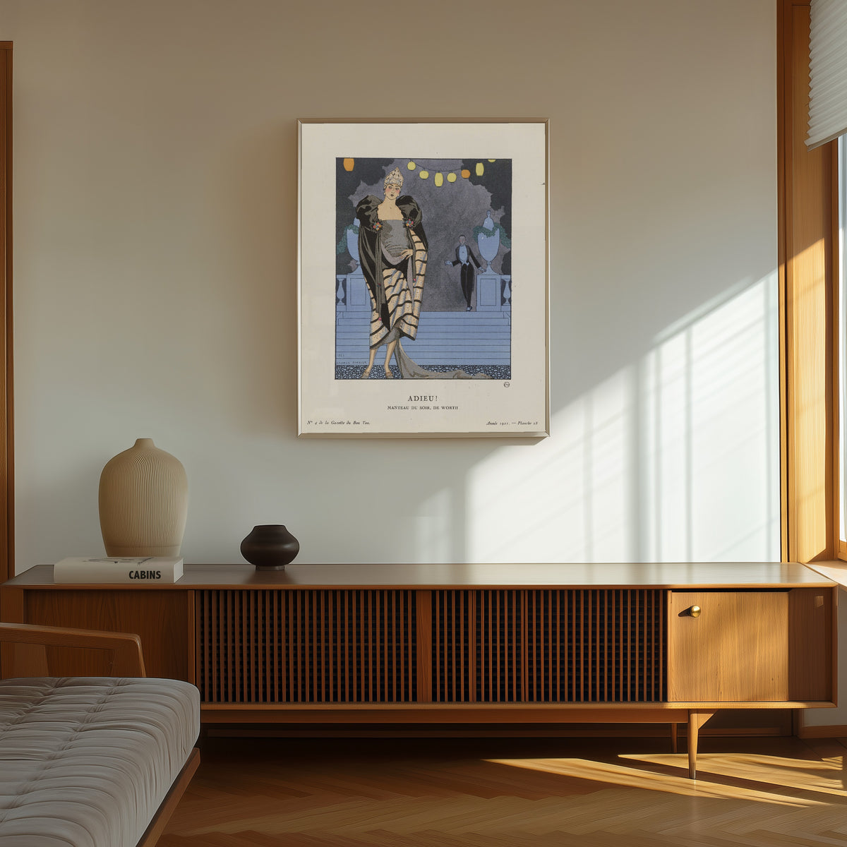 Framed art print of Adieu! Manteau du soir de Worth by George Barbier, in a thin light frame on a sunlit wall above a wooden sideboard
