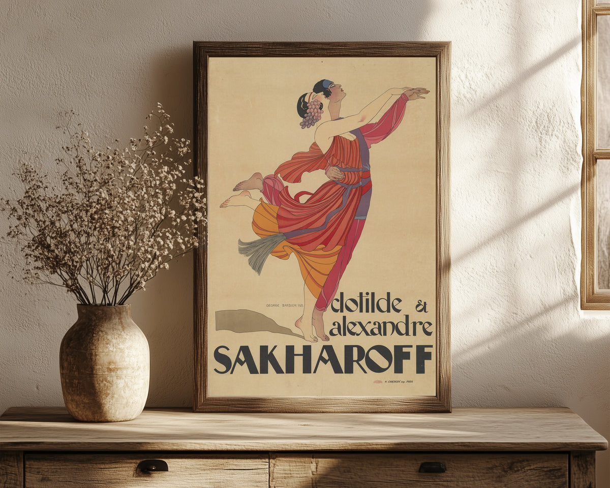 Framed art print of Clotilde et Alexandre Sakharoff by George Barbier, in a dark wood frame leaning on a rustic console beside dried flowers