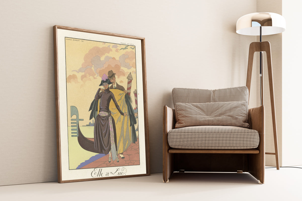 Elle et Lui by George Barbier — framed and leaning against a wall beside an armchair and a floor lamp