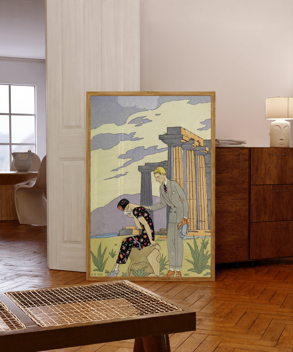 Framed art print of Falbalas et Fanfreluches: Paestum by George Barbier, in a light wood frame leaning in a warm room with a parquet floor
