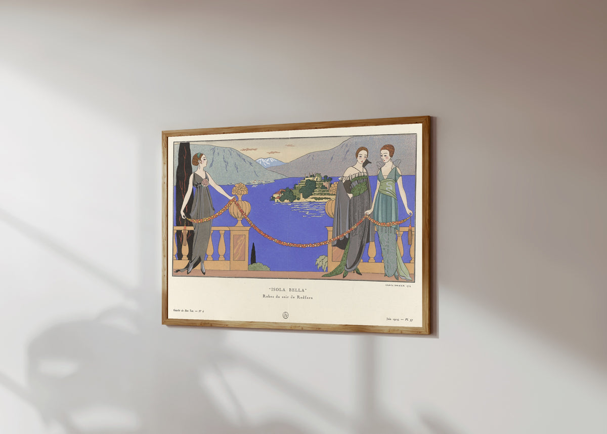 Framed art print of Isola Bella, robes du soir de Redfern by George Barbier, in a light wood frame on a sunlit white wall, seen at a slight angle