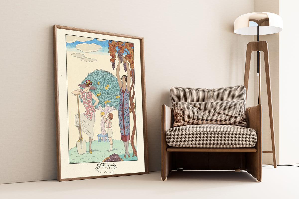 La Terre by George Barbier — framed and leaning against a wall beside an armchair and a floor lamp
