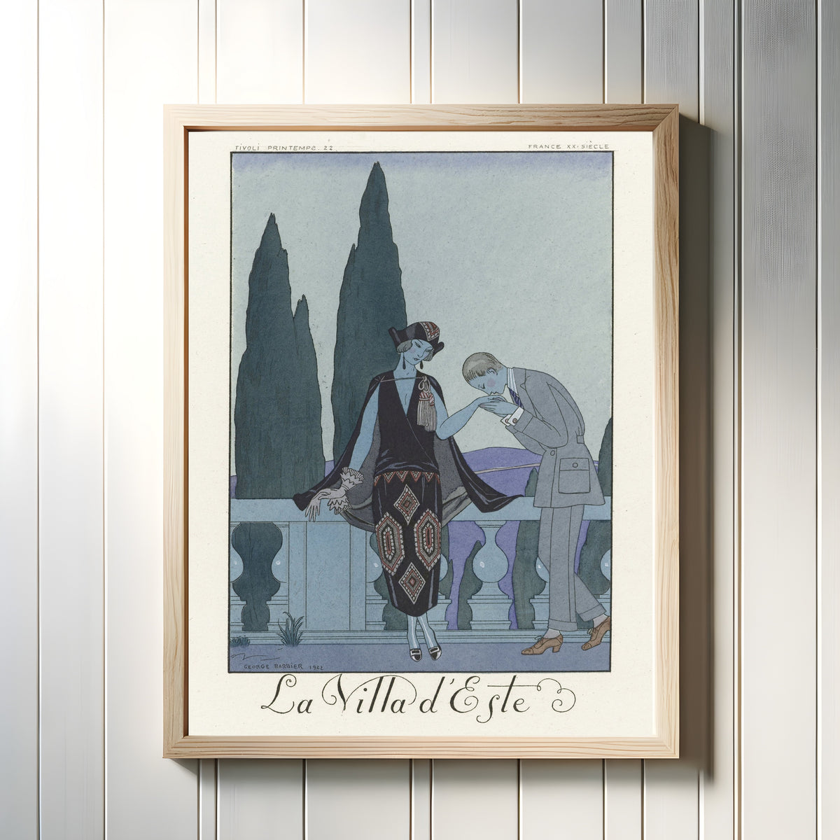 Framed art print of La Villa d'Este by George Barbier, in a light wood frame on a white panelled wall