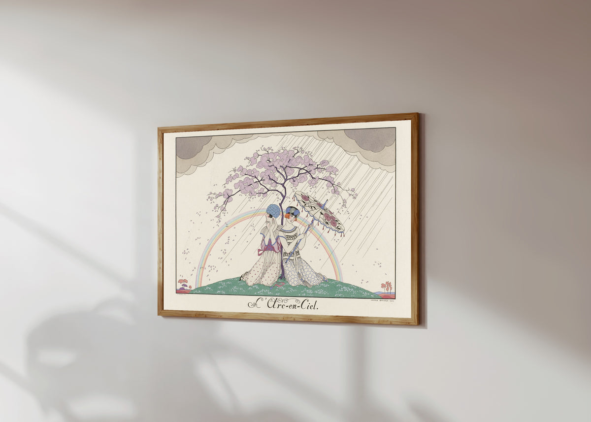 Framed art print of L'Arc-en-ciel [The Rainbow] by George Barbier, in a light wood frame on a sunlit white wall, seen at a slight angle