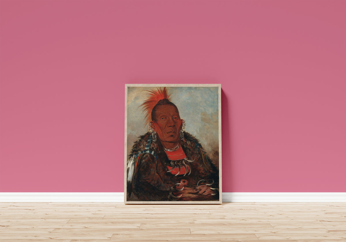 Framed art print of Wah-ro-née-sah, The Surrounder, Chief of the Tribe by George Catlin, in a light wood frame leaning on a pink wall above a wooden floor