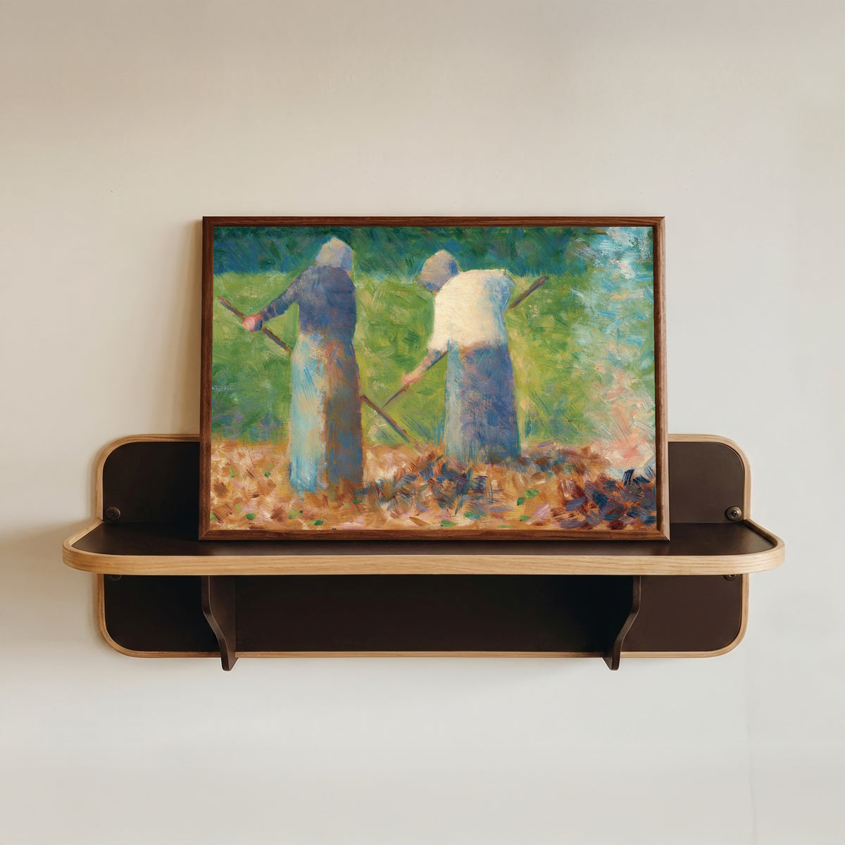 Framed art print of Haymakers at Montfermeil by Georges Seurat, in a dark wood frame resting on a wall shelf