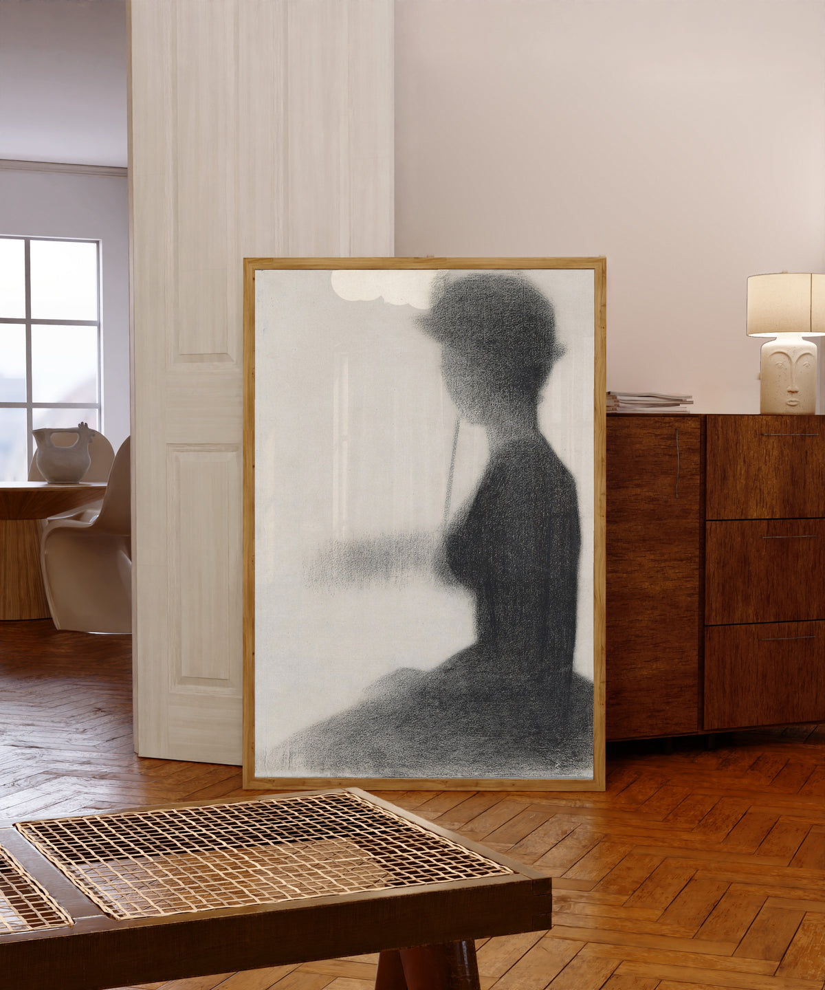 Framed art print of Seated Woman with a Parasol (study for La Grande Jatte) by Georges Seurat, in a light wood frame leaning in a warm room with a parquet floor