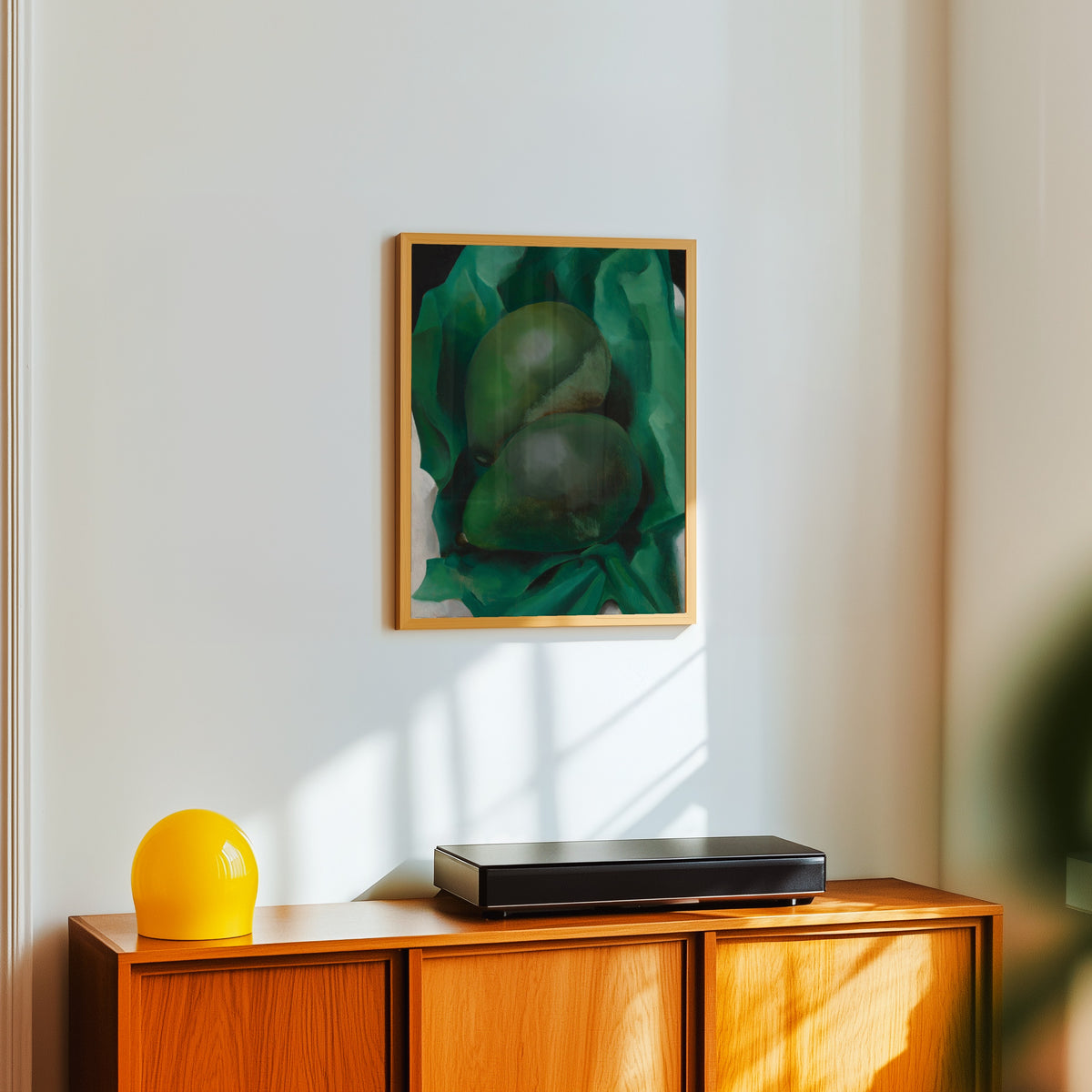 Framed art print of Alligator Pears by Georgia O'Keeffe, in a light wood frame on a white wall above an orange sideboard