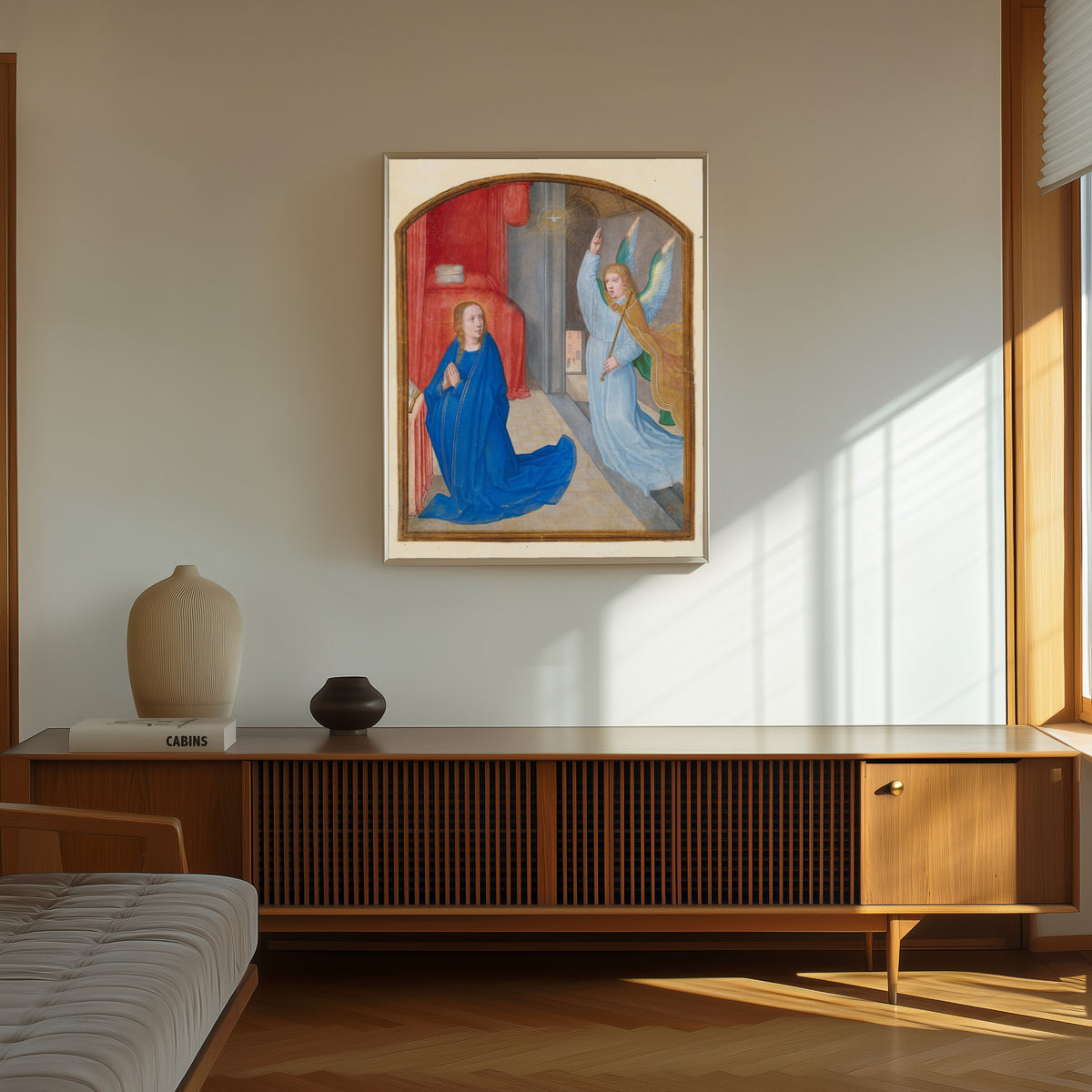 Framed art print of The Annunciation by Gerard David (circle of), in a thin light frame on a sunlit wall above a wooden sideboard