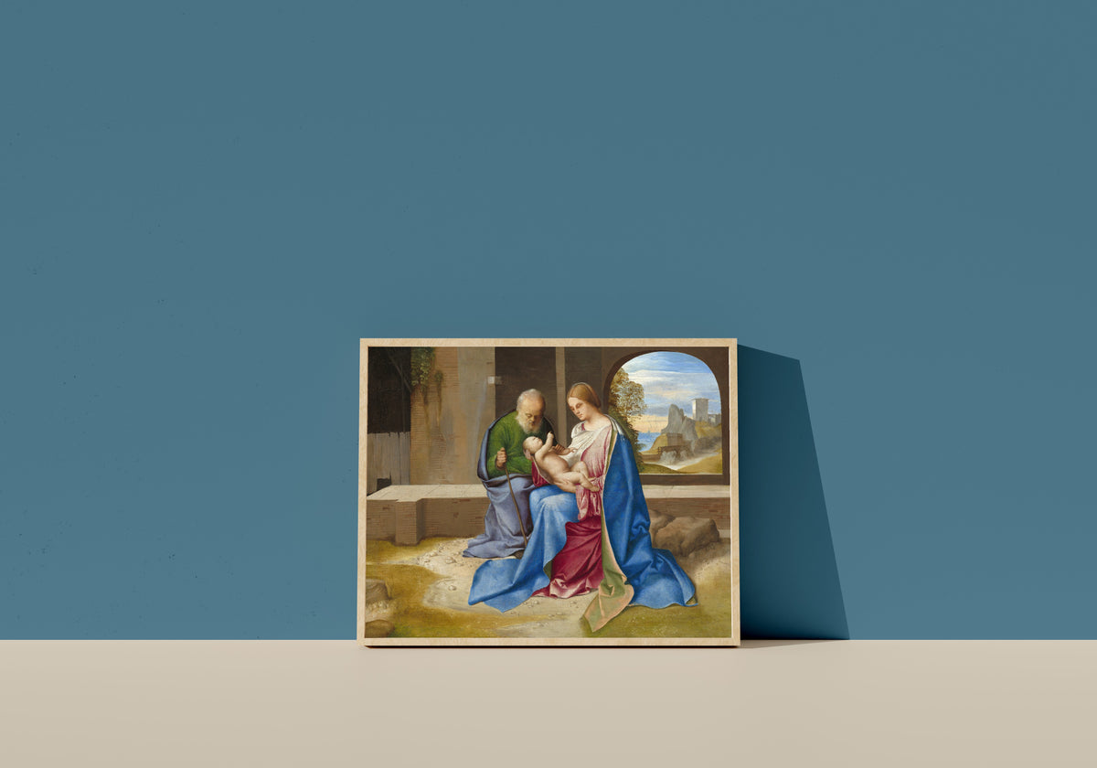 Framed art print of The Holy Family by Giorgione, in a light wood frame leaning on a blue wall