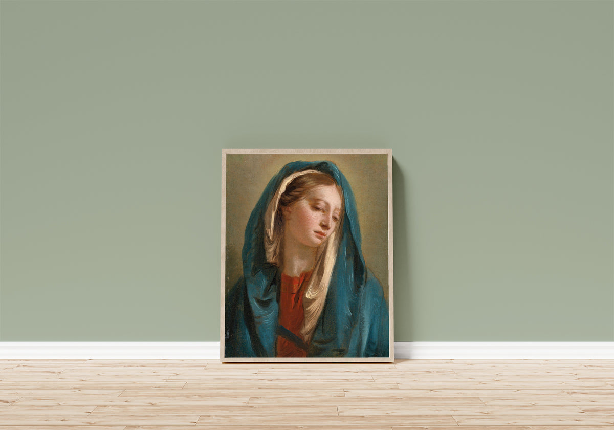 Framed art print of The Madonna Facing Front and Wearing… by Giovanni Battista Tiepolo, in a light wood frame leaning on a sage green wall above a wooden floor