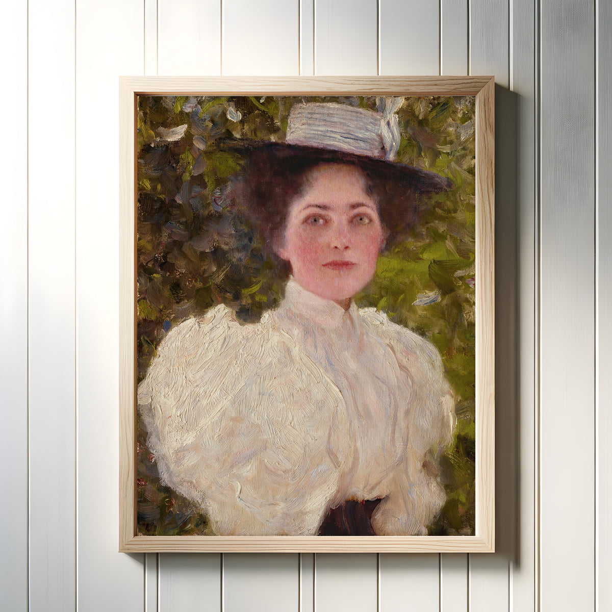 Framed art print of Girl in the Foliage (Mädchen im Grünen) by Gustav Klimt, in a light wood frame on a white panelled wall