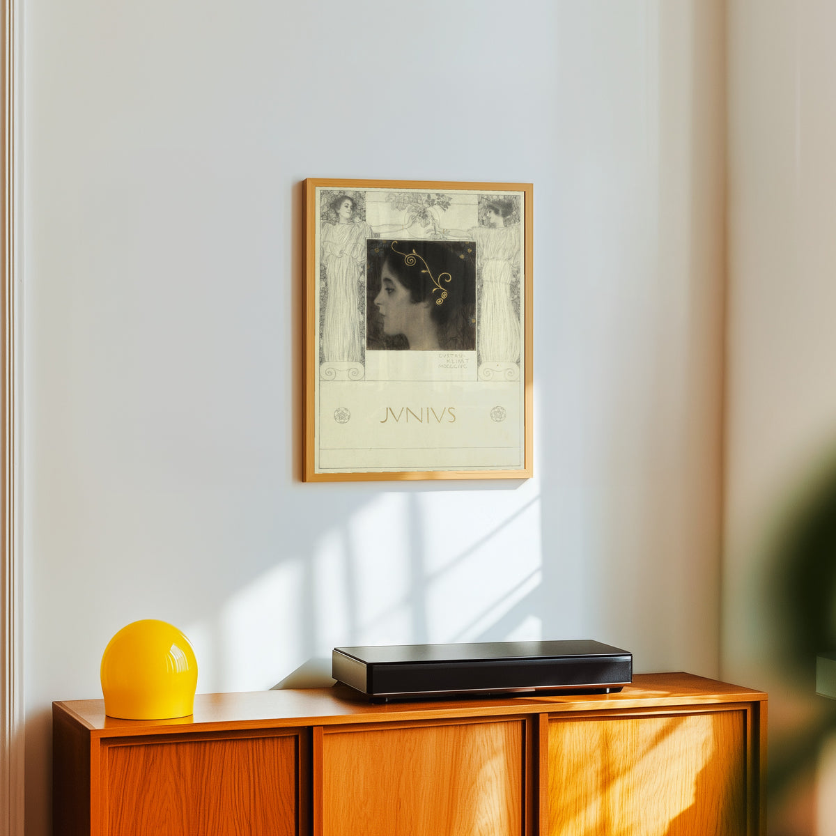 Framed art print of Junius by Gustav Klimt, in a light wood frame on a white wall above an orange sideboard