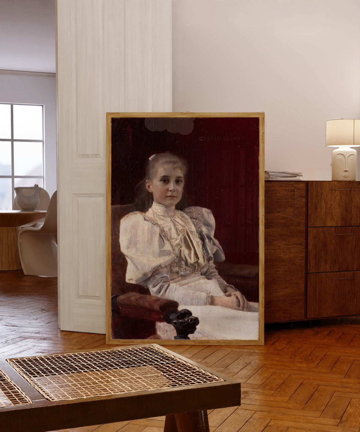 Framed art print of Seated Young Girl by Gustav Klimt, in a light wood frame leaning in a warm room with a parquet floor