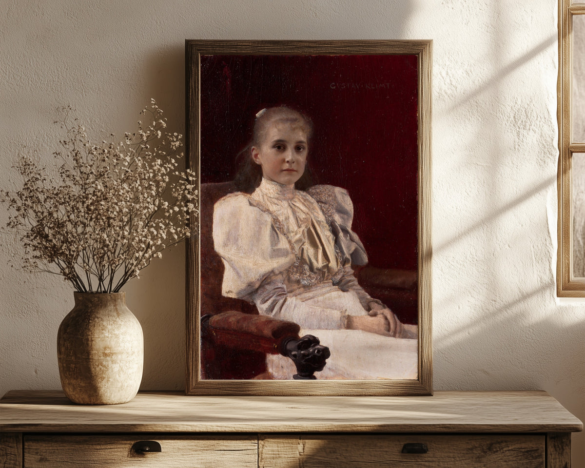 Framed art print of Seated Young Girl by Gustav Klimt, in a dark wood frame leaning on a rustic console beside dried flowers