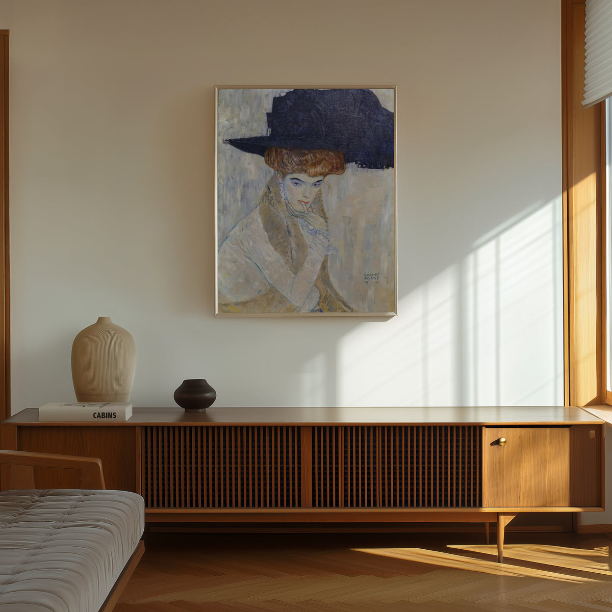 Framed art print of The Black Feathered Hat by Gustav Klimt, in a thin light frame on a sunlit wall above a wooden sideboard