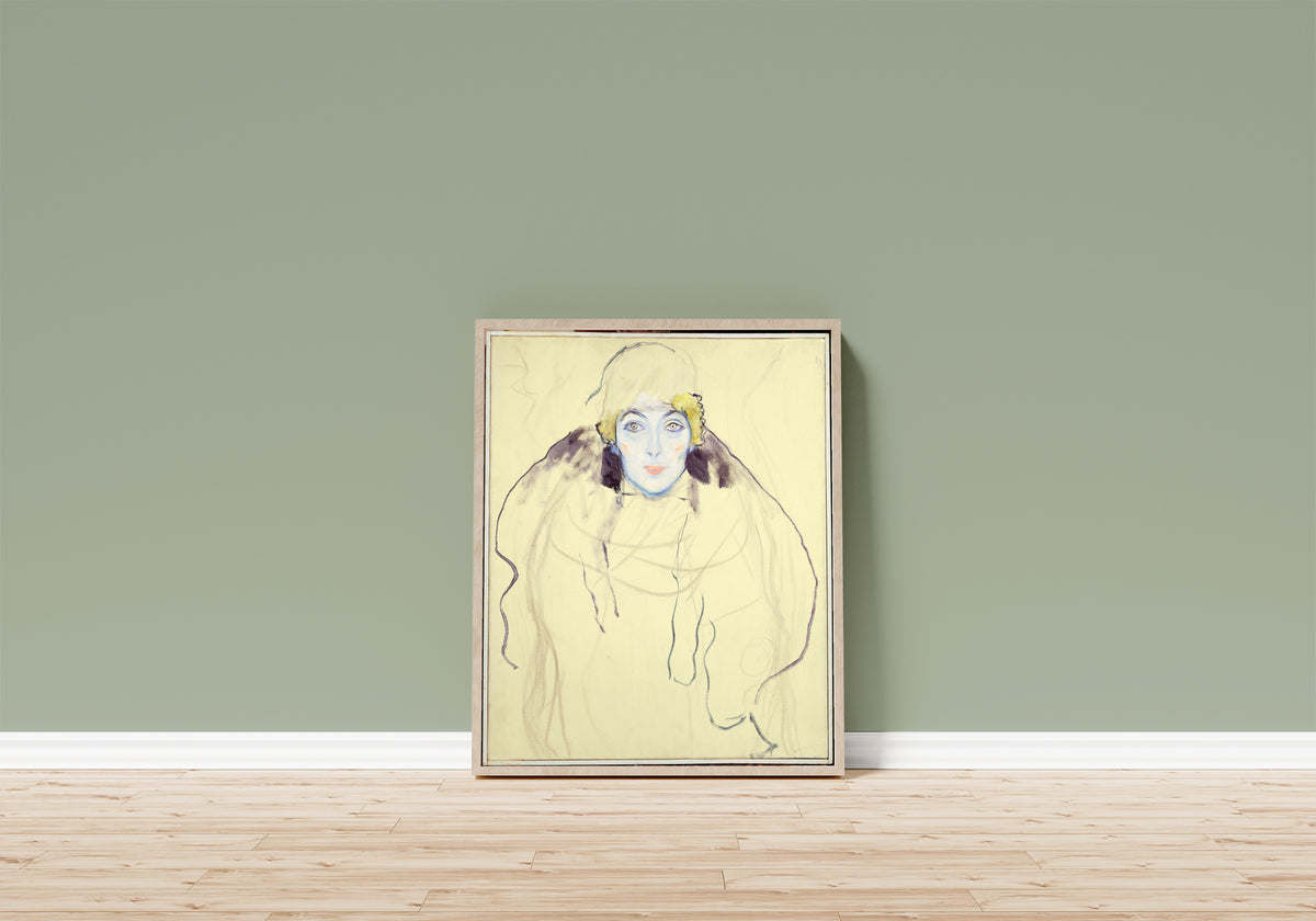 Framed art print of Woman's Head by Gustav Klimt, in a light wood frame leaning on a sage green wall above a wooden floor