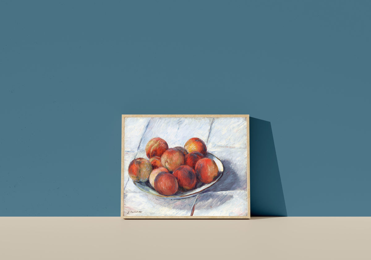 Framed art print of L’Assiette de pêches (Plate of Peaches) by Gustave Caillebotte, in a light wood frame leaning on a blue wall