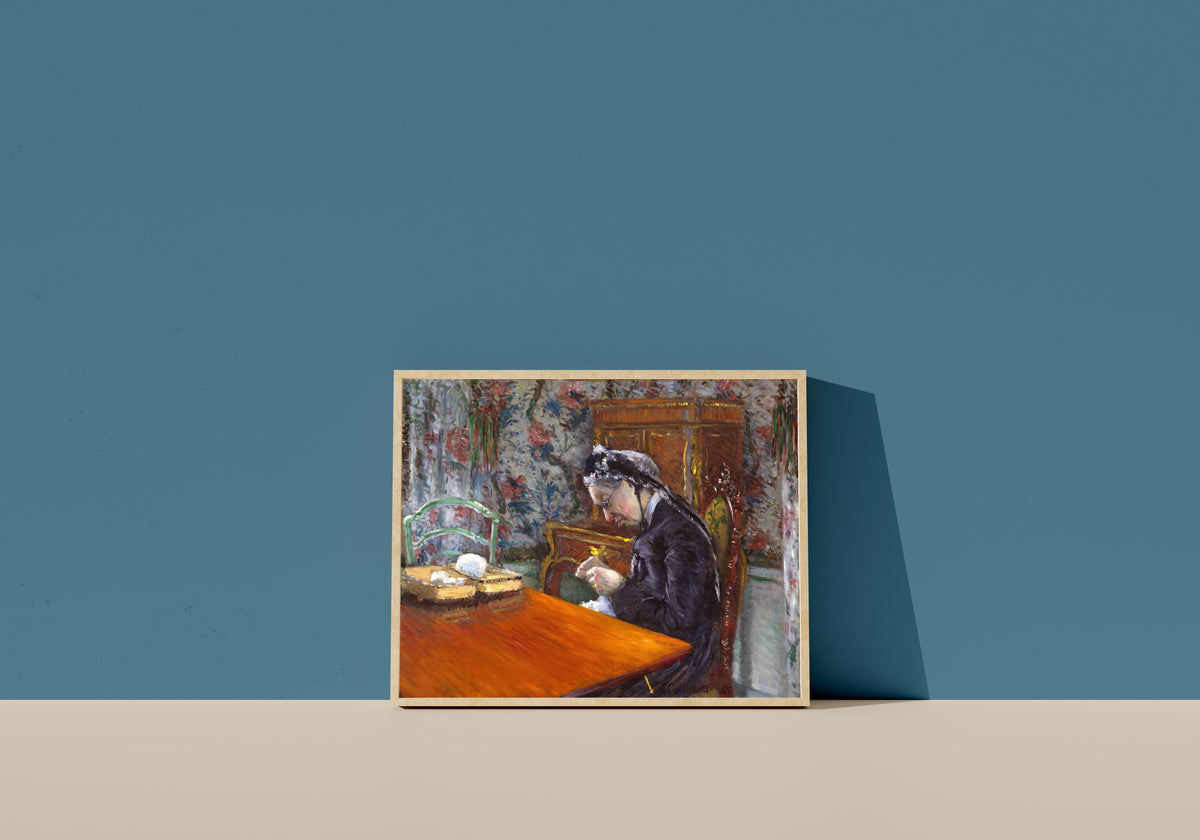 Framed art print of Mademoiselle Boissière Knitting by Gustave Caillebotte, in a light wood frame leaning on a blue wall