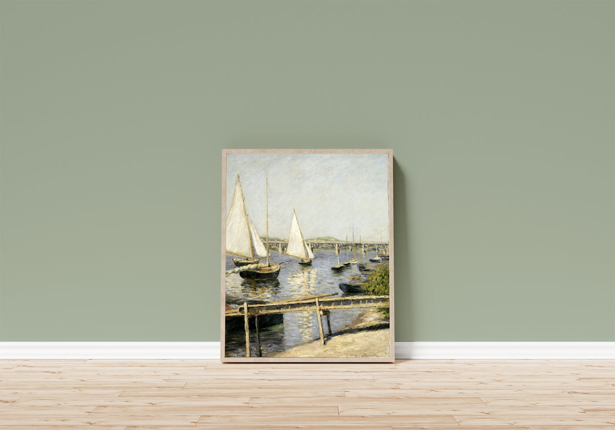 Framed art print of Sailing Boats at Argenteuil by Gustave Caillebotte, in a light wood frame leaning on a sage green wall above a wooden floor