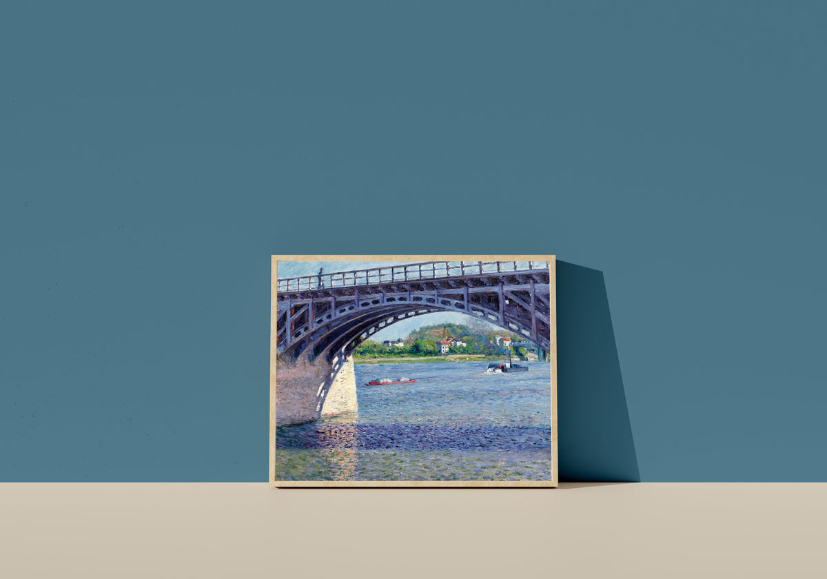 Framed art print of The Argenteuil Bridge and the Seine by Gustave Caillebotte, in a light wood frame leaning on a blue wall