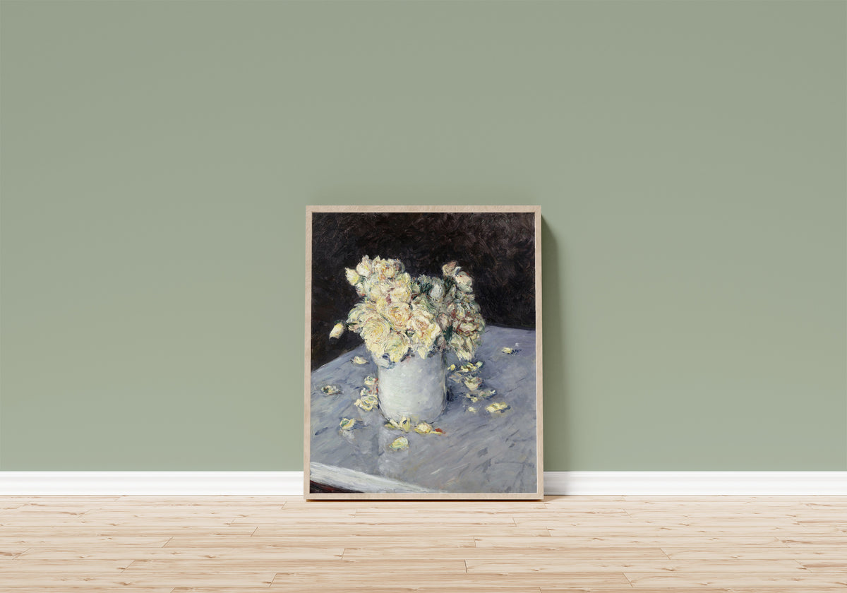 Framed art print of Yellow Roses in a Vase by Gustave Caillebotte, in a light wood frame leaning on a sage green wall above a wooden floor