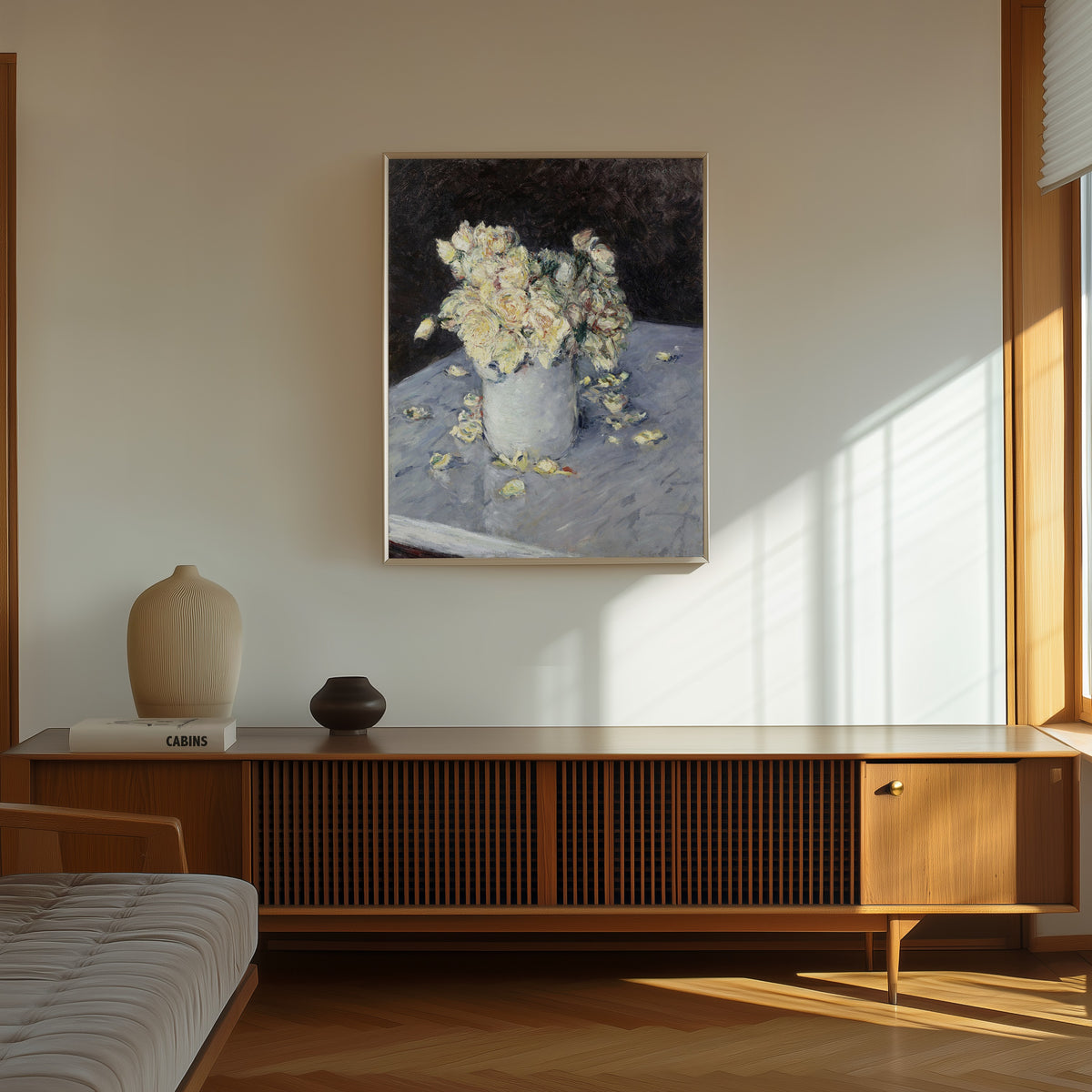 Framed art print of Yellow Roses in a Vase by Gustave Caillebotte, in a thin light frame on a sunlit wall above a wooden sideboard