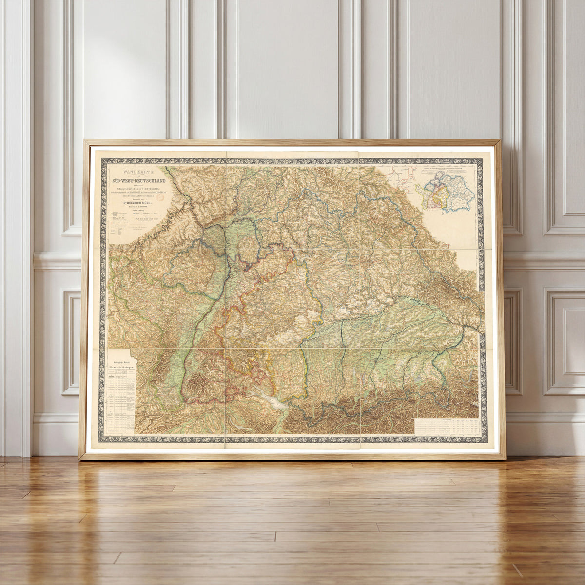 Framed art print of Wall Map of South-West Germany (Wandkarte von… by Heinrich Moehl, in a light wood frame leaning against a panelled white wall