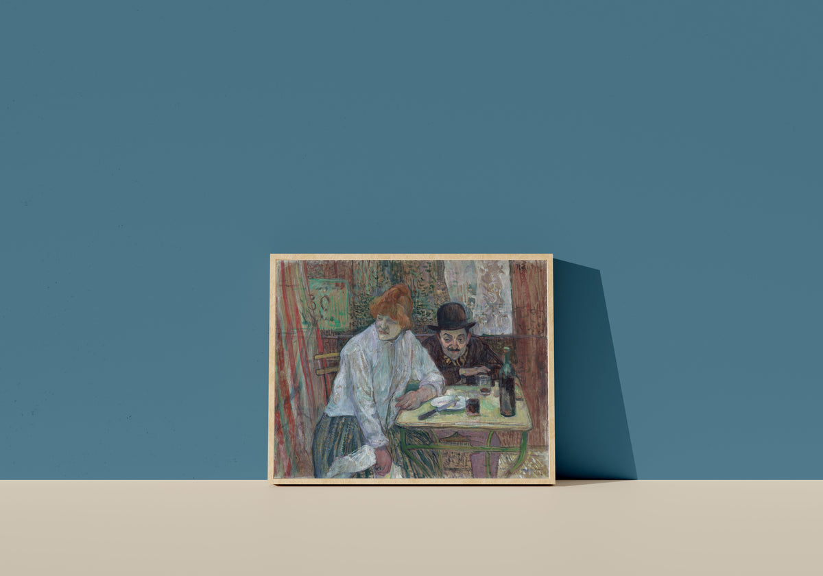 Framed art print of At the Café La Mie by Henri de Toulouse-Lautrec, in a light wood frame leaning on a blue wall