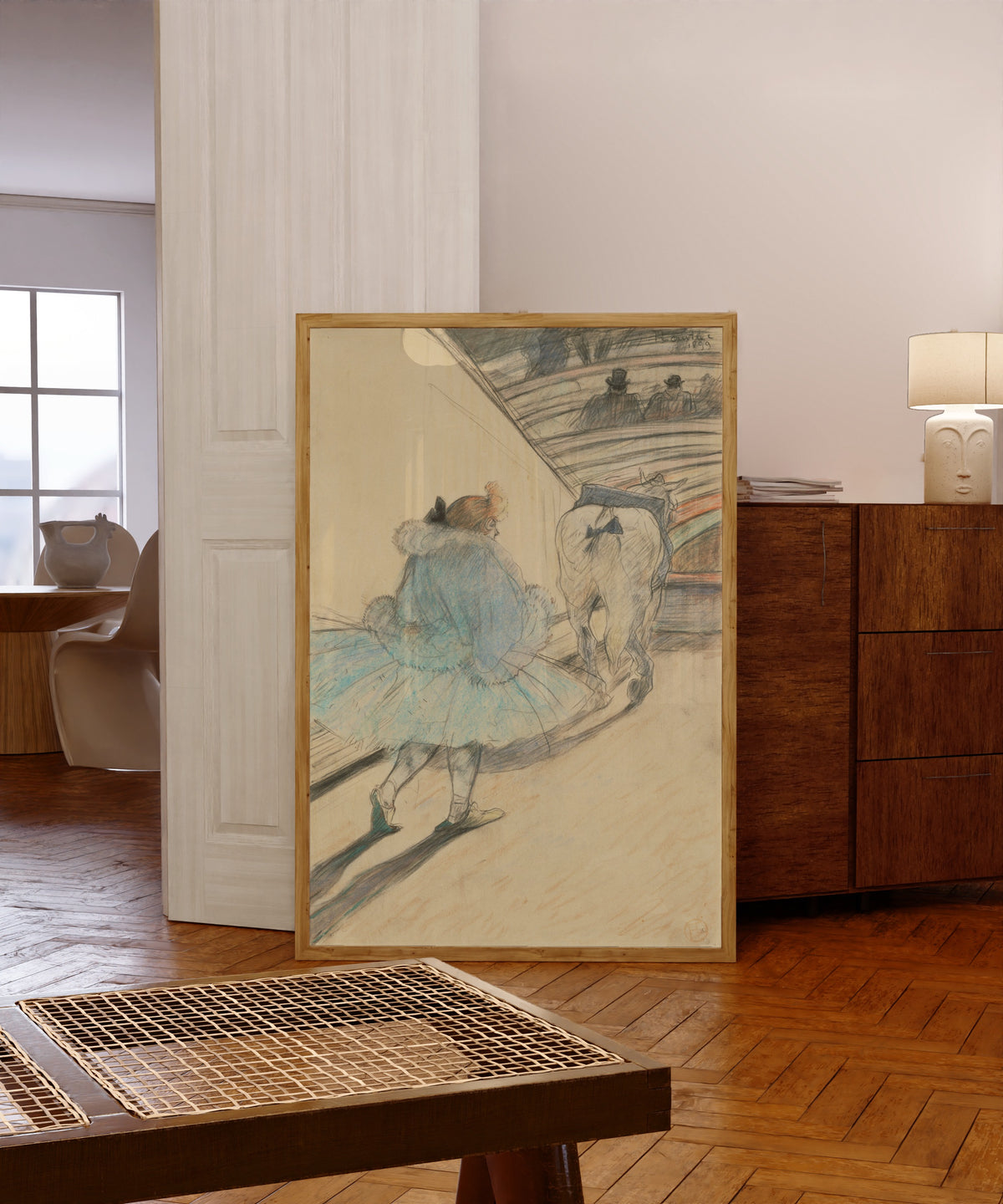 Framed art print of At the Circus: Entering the Ring by Henri de Toulouse-Lautrec, in a light wood frame leaning in a warm room with a parquet floor