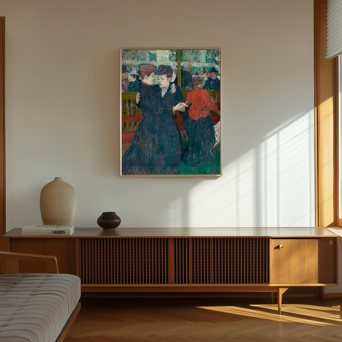Framed art print of At the Moulin Rouge: Two Women Waltzing by Henri de Toulouse-Lautrec, in a thin light frame on a sunlit wall above a wooden sideboard