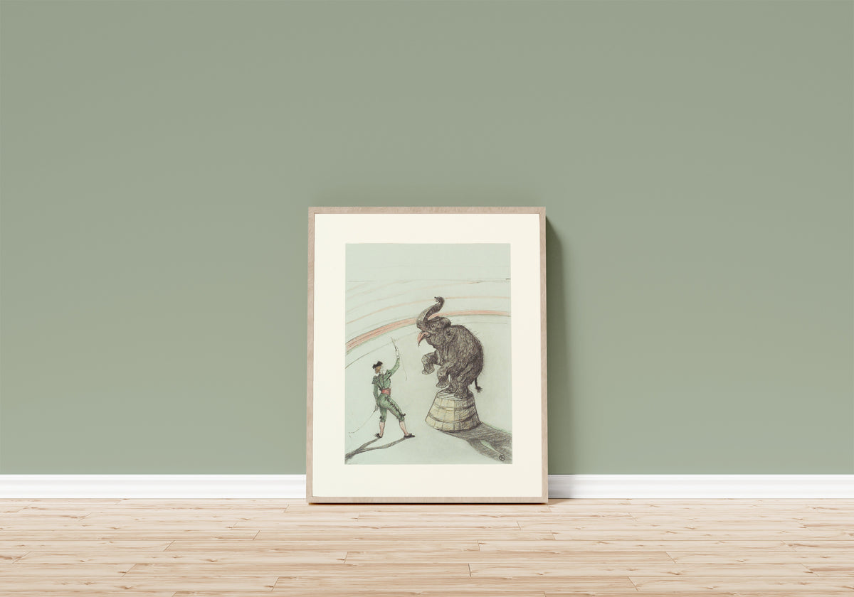 Framed art print of Au Cirque: Éléphant en liberté by Henri de Toulouse-Lautrec, in a light wood frame leaning on a sage green wall above a wooden floor
