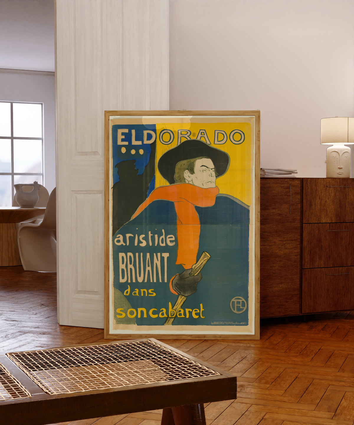 Framed art print of Eldorado: Aristide Bruant by Henri de Toulouse-Lautrec, in a light wood frame leaning in a warm room with a parquet floor