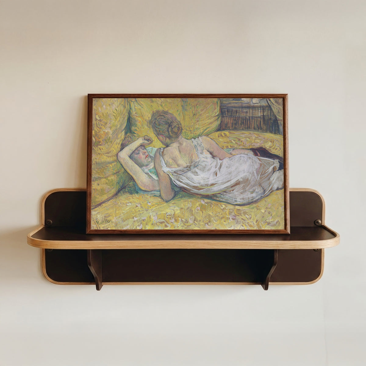 Framed art print of L'Abandon (Les Deux Amies) by Henri de Toulouse-Lautrec, in a dark wood frame resting on a wall shelf