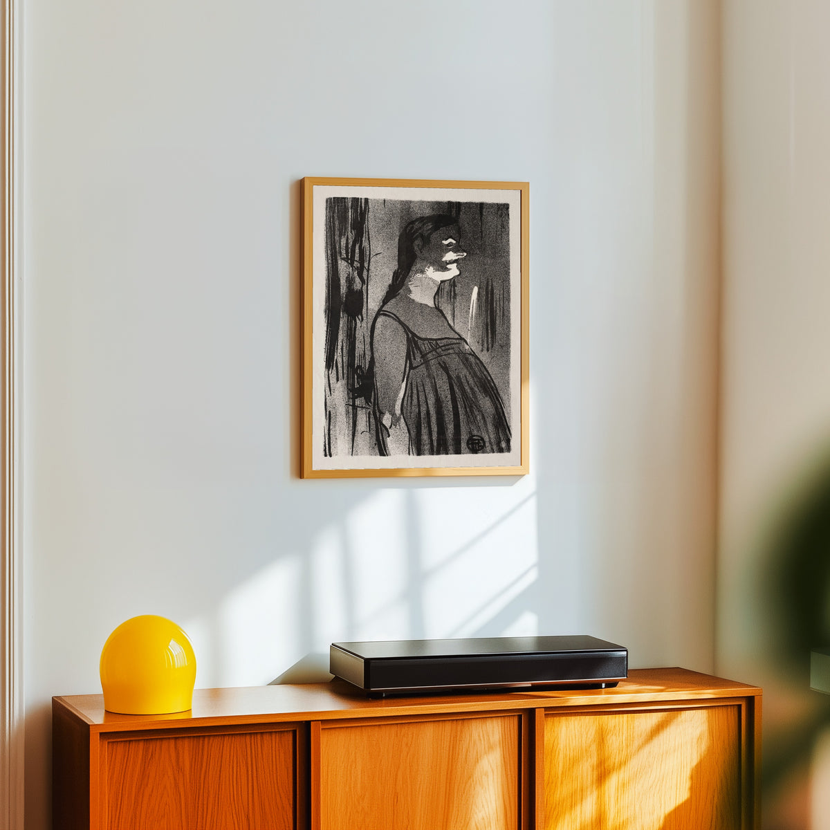 Framed art print of Le Café-Concert: Mme. Abdala by Henri de Toulouse-Lautrec, in a light wood frame on a white wall above an orange sideboard