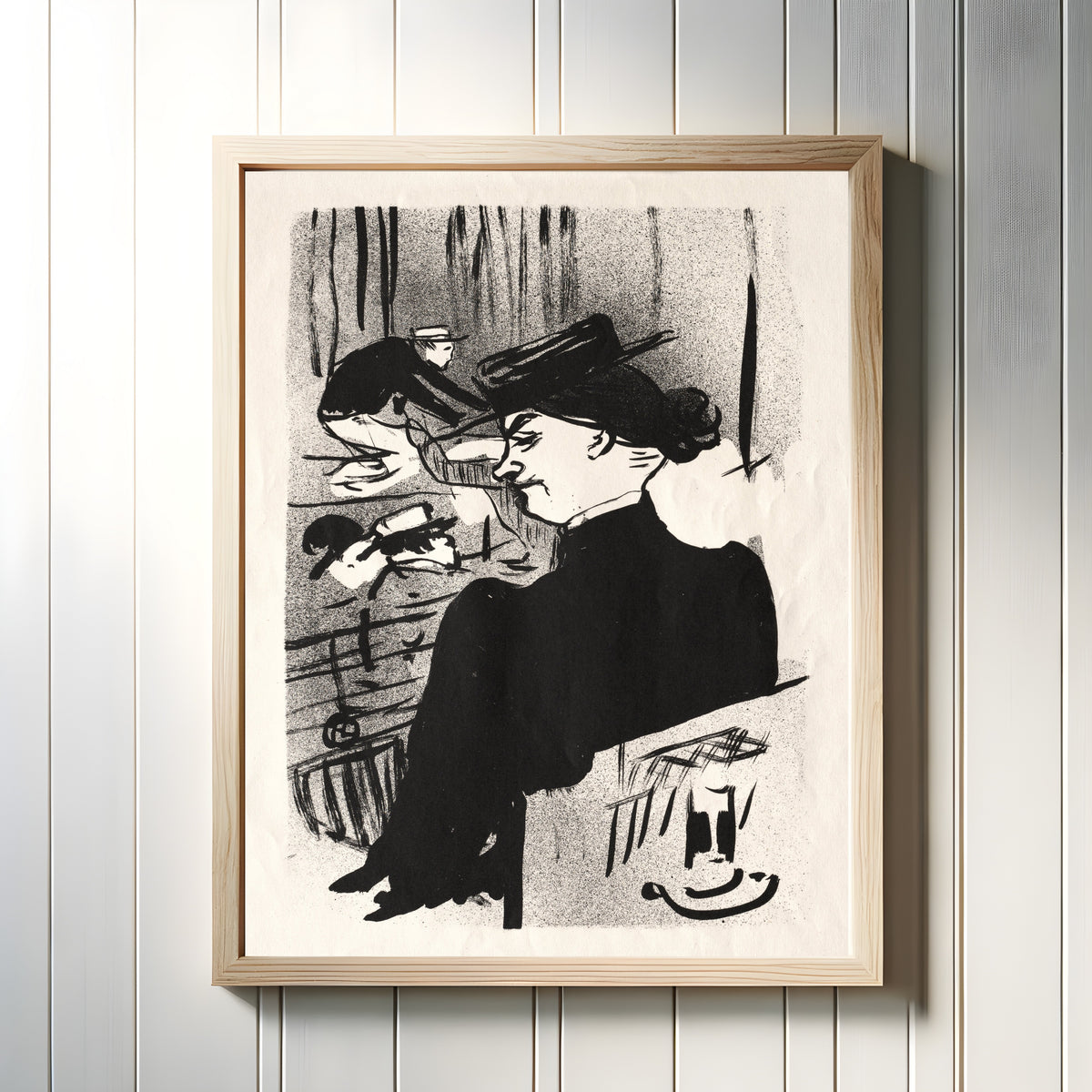 Framed art print of Le Café-Concert: Une Spectatrice by Henri de Toulouse-Lautrec, in a light wood frame on a white panelled wall