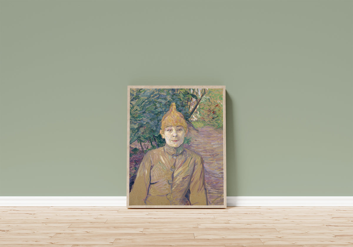 Framed art print of The Streetwalker by Henri de Toulouse-Lautrec, in a light wood frame leaning on a sage green wall above a wooden floor