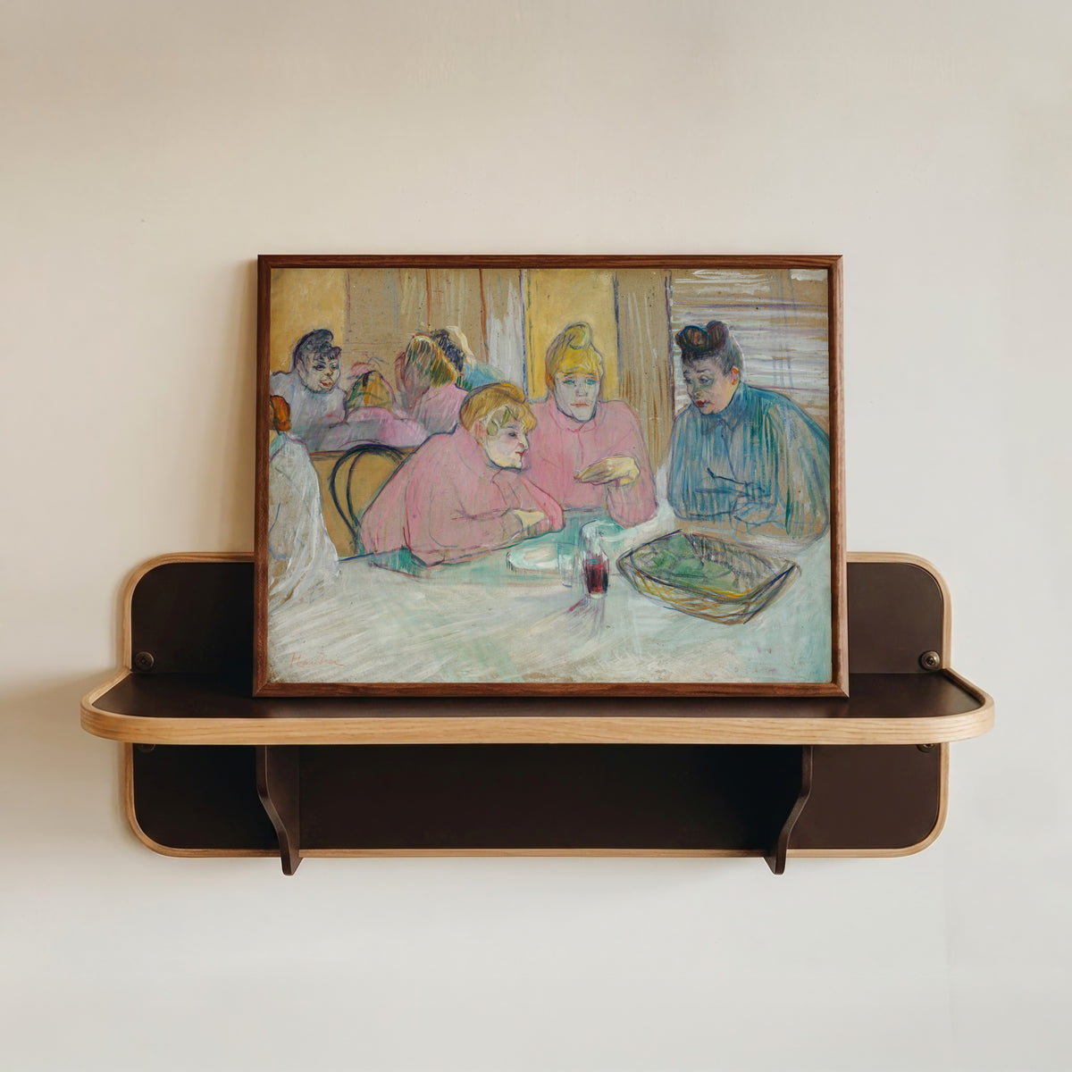 Framed art print of These Ladies in the Dining Room by Henri de Toulouse-Lautrec, in a dark wood frame resting on a wall shelf
