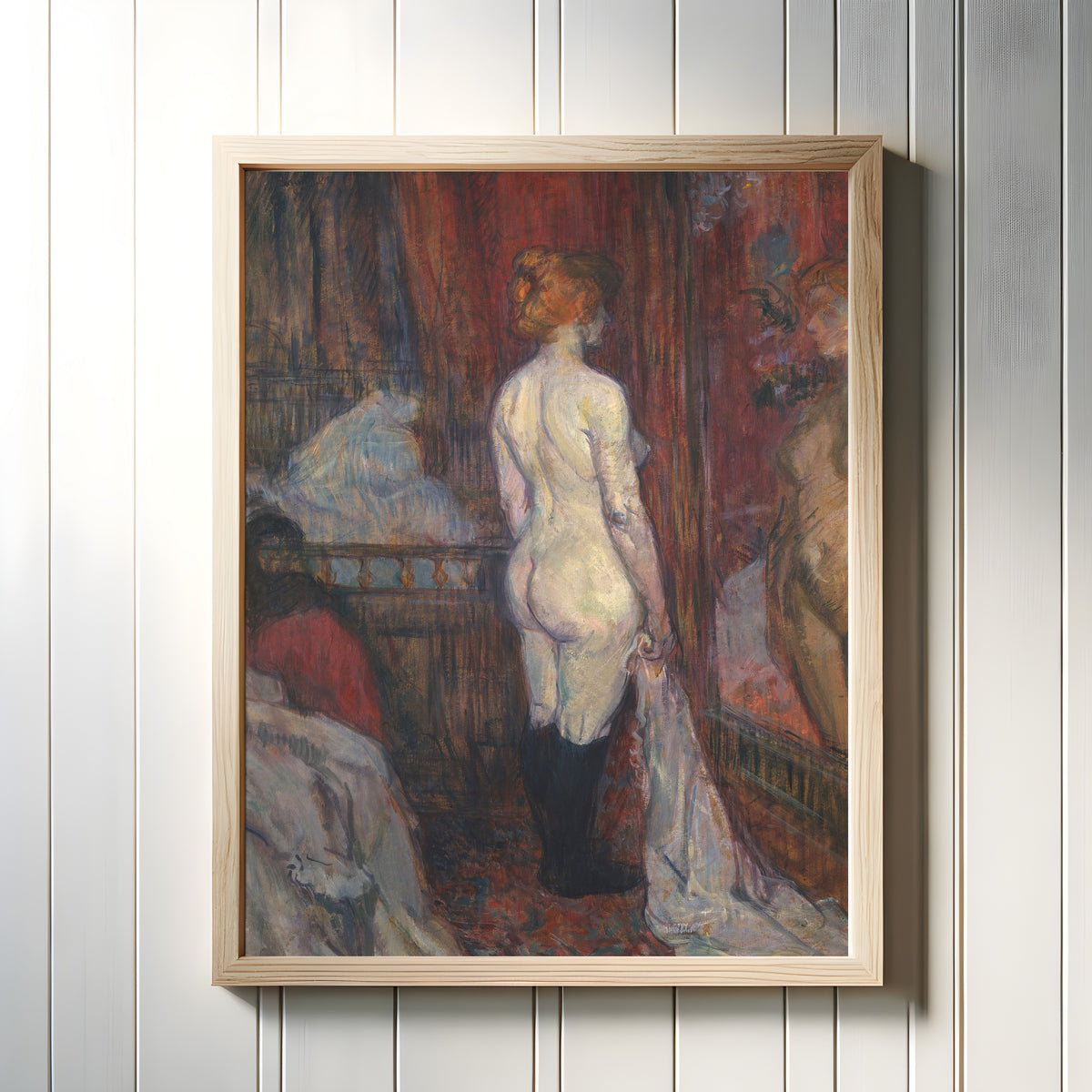Framed art print of Woman before a Mirror by Henri de Toulouse-Lautrec, in a light wood frame on a white panelled wall