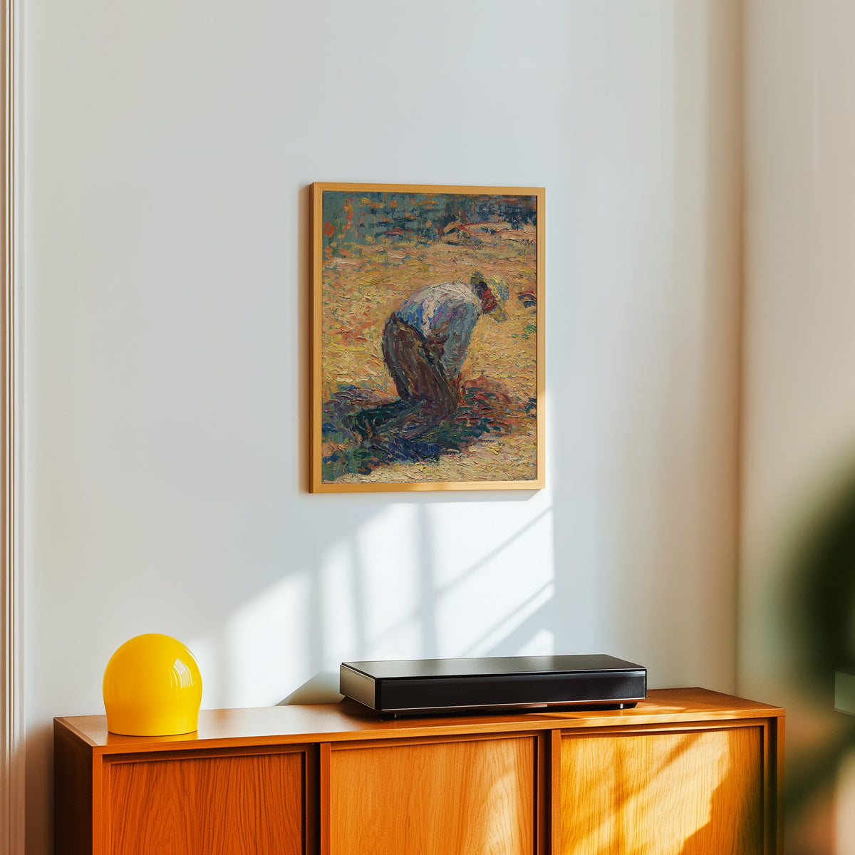 Framed art print of Étude pour La Moisson (Crouching Harvester) by Henri Martin, in a light wood frame on a white wall above an orange sideboard