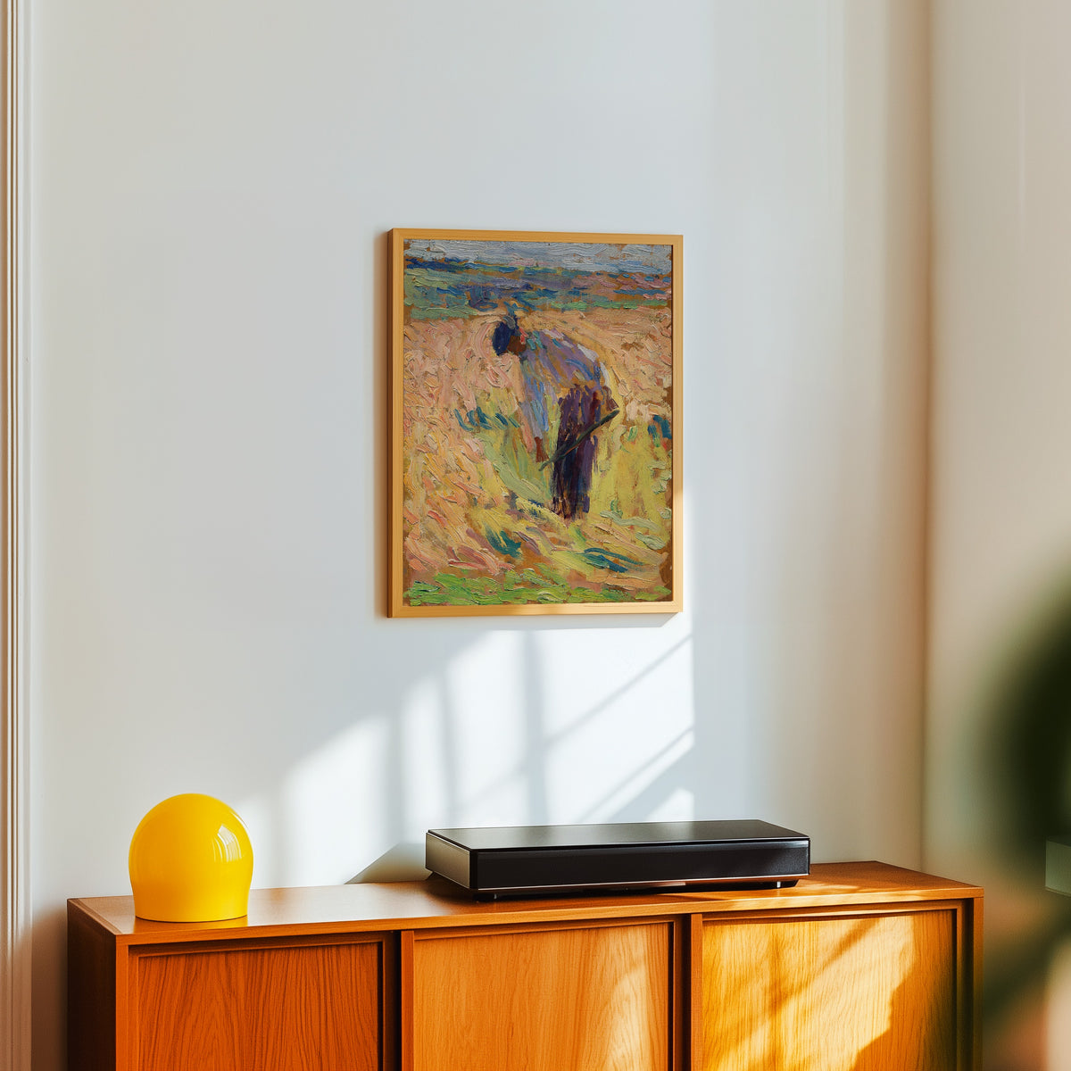 Framed art print of Étude pour La Moisson (Standing Harvester) by Henri Martin, in a light wood frame on a white wall above an orange sideboard