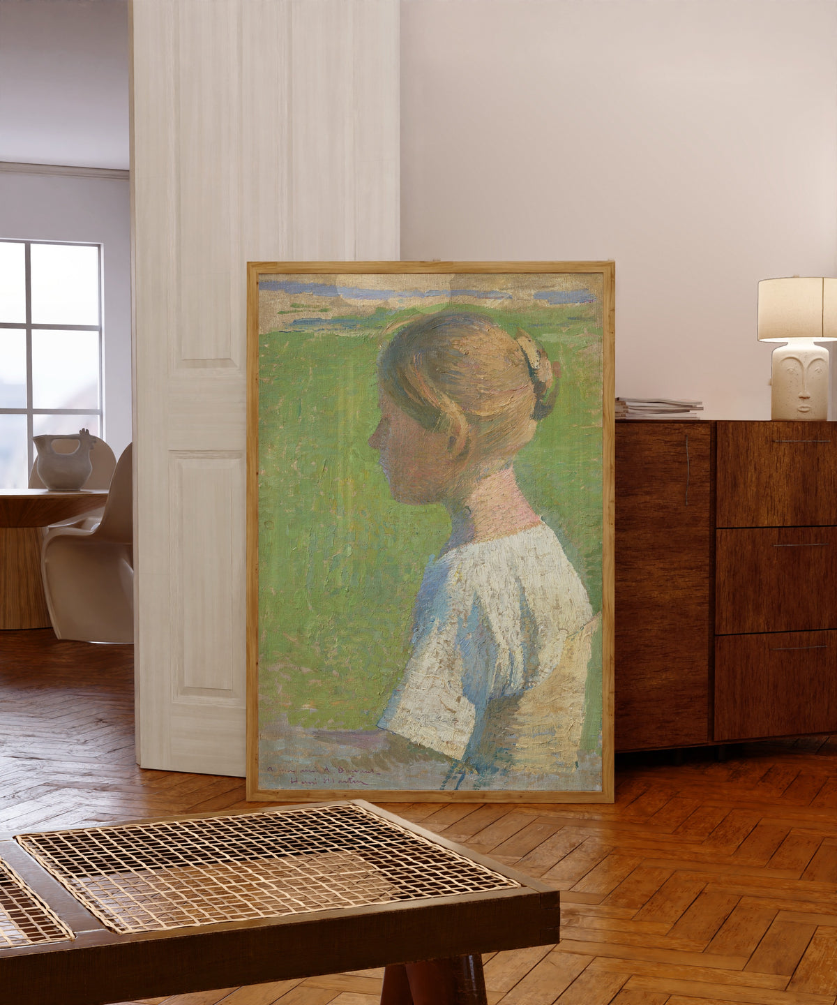 Framed art print of Jeune femme de profil by Henri Martin, in a light wood frame leaning in a warm room with a parquet floor